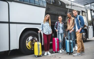 multicultural friends with travels bags posing near travel bus at street