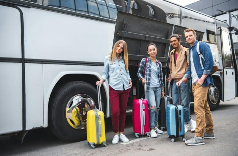 multicultural friends with travels bags posing near travel bus at street